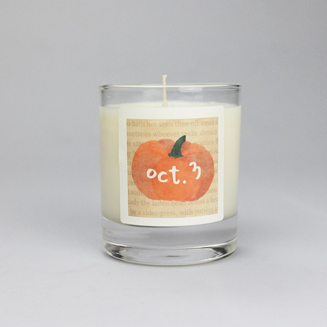 Product photo of scented soy candle Oct. 3, made by BONKI. Candle in glass jar. Beige label with orange pumpkin and writing "Oct. 3".