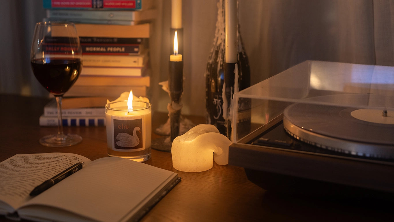 Scented candle Elio by night, with record player, note book and glass of red wine.
