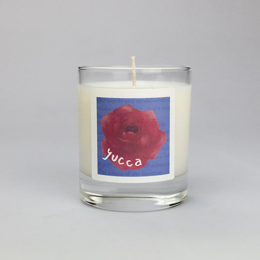 Product photo of scented soy candle Yucca, made by BONKI. Candle in glass jar. Blue label with red rose and writing "Yucca".